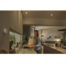 Bílý detektor pohybu na stěně v moderní kuchyni se ženou nesoucí nákupní tašku.