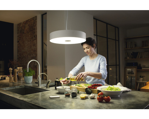 Žena připravuje salát pod kulatým stropním svítidlem v kuchyni