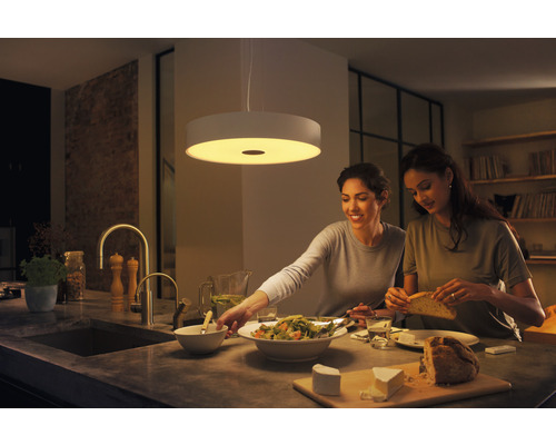 Dvě ženy připravují jídlo v jasné kuchyni pod kulatým závěsným světlem.