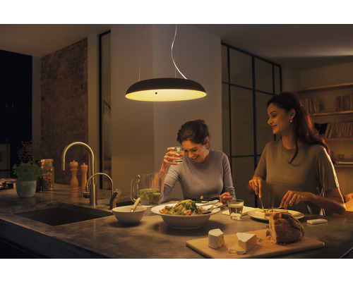 Dvě ženy sedí u kuchyňského stolu pod závěsným svítidlem a jedí.