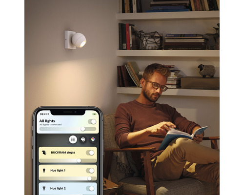 Scéna obývacího pokoje s mužem čtoucím knihu a nástěnným svítidlem ovládaným aplikací