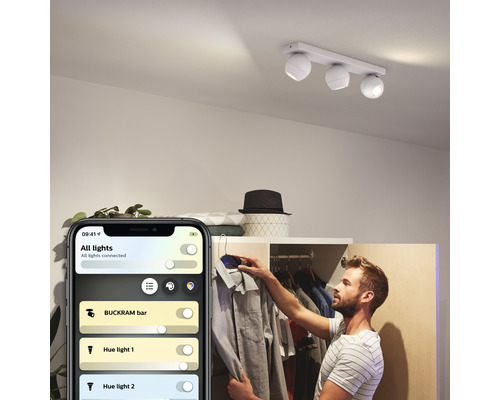 Scéna muže ovládajícího stropní svítidlo Philips Hue Buckram pomocí aplikace pro smartphone
