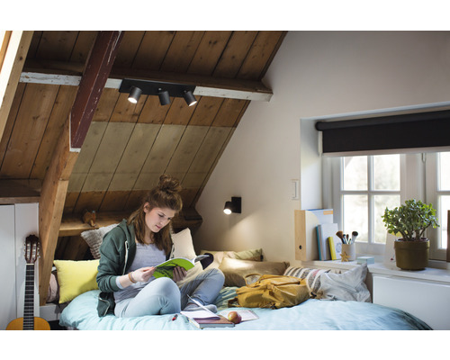 Útulný podkrovní pokoj s dřevěným stropem a stropním svítidlem, kde mladá žena čte v posteli