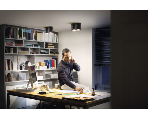 Muž sedí na stole v pracovně se stropními svítidly a policemi