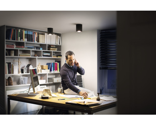 Muž telefonuje na stole pod stropními svítidly v pracovně.