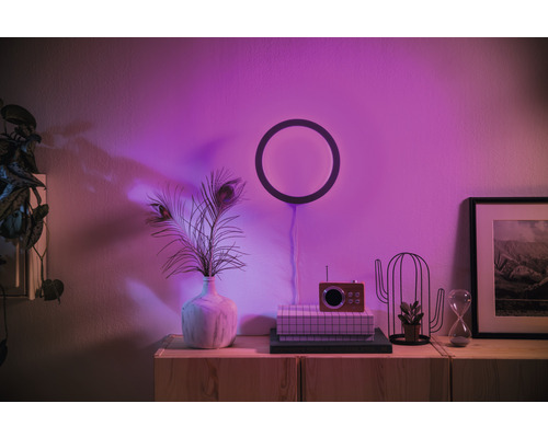 Obývací pokoj s kruhovým nástěnným svítidlem, váza s pavími pery a dekorativními prvky na skříňce.