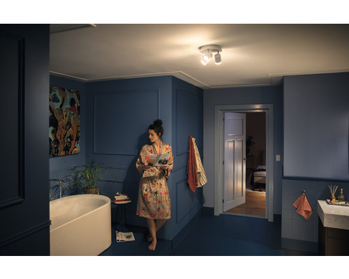 Koupelna s vanou, stropním svítidlem a ženou čtoucí časopis