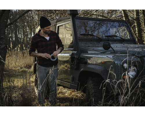 Muž s lepicí páskou vedle terénního vozidla v terénu.