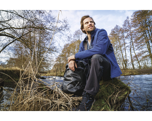 Muž sedí s batohem na břehu potoka v přírodě.