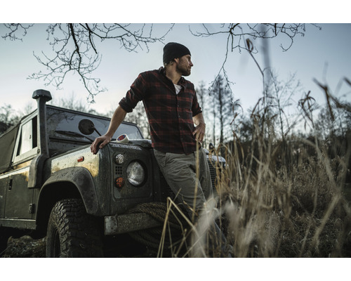 Muž v kostkované košili se opírá o terénní auto v přírodním prostředí