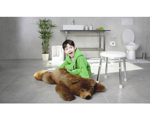 Světlá koupelna s chlapcem v županu sedícím vedle medvěda na stoličce, s umyvadlem, toaletou a rostlinou