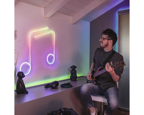 Muž hraje na kytaru před svítící notou jako dekorací na zeď