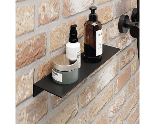 Černá nástěnná police v koupelně s pečujícími produkty na pozadí z cihel.