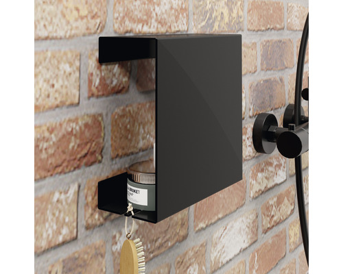 Černá sprchová polička na cihlové zdi se štětcem a plechovkou