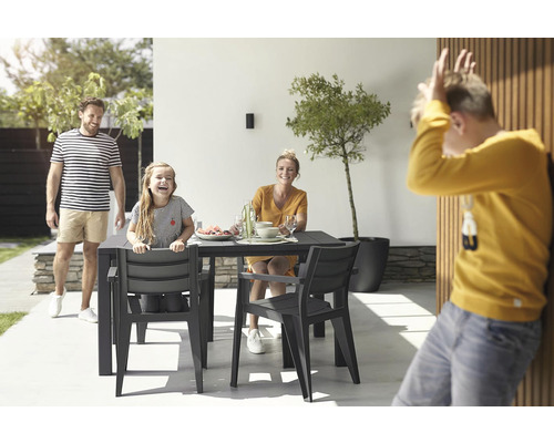 Rodina sedí venku u zahradního stolu se židlemi