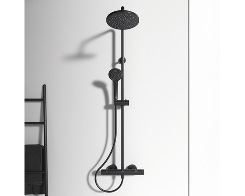 Černá sprchová armatura s hlavovou a ruční sprchou namontovaná na zdi.