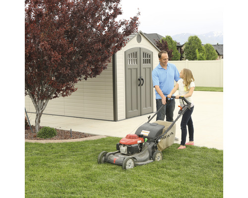 Otec a dcera sekají trávník sekačkou před zahradním domkem.