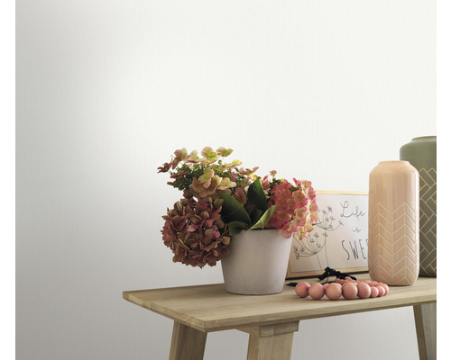 Detail zdobeného dřevěného stolu s květinami, vázami a rámem na fotografie před bílou zdí