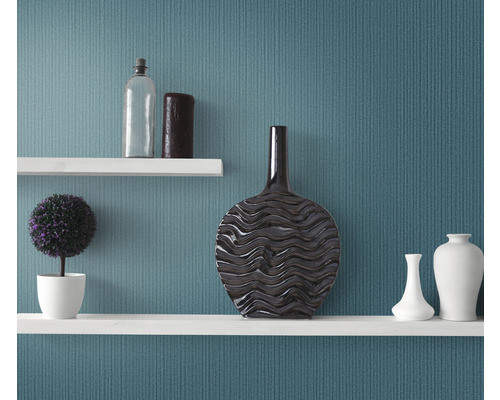 Dekorativní police s vázami, rostlinou a lahví před stěnou