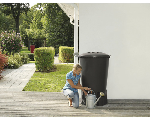 Žena plní konev u sudu na dešťovou vodu na zahradě