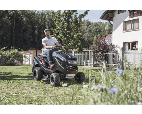 Muž jede na zahradním traktoru na trávníku před domem
