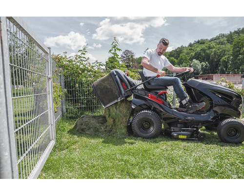 Muž vysypává koš na trávu zahradního traktoru na trávník