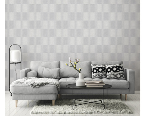 Světlý obývací pokoj s šedou pohovkou, stolem a vzorovanou tapetou pro přátelskou atmosféru.