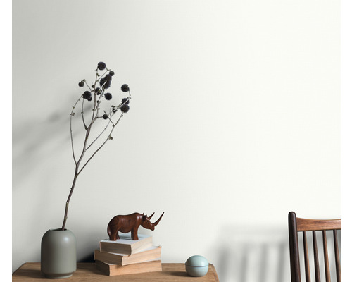 Obývací pokoj s aranžmá vázy, dekorativního objektu a stohu knih před natřenou stěnou.