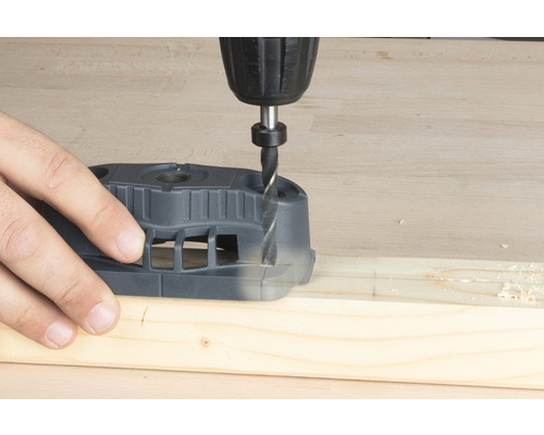 Vrtačka vrtá otvor do dřevěné desky pomocí vrtací šablony.