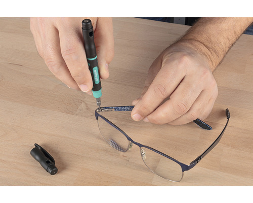 Osoba opravuje brýle pomocí šroubováku