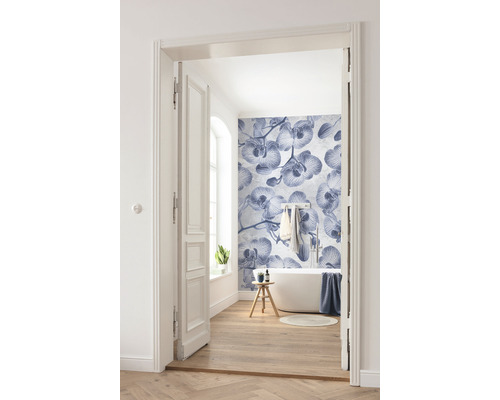 Světlá koupelna s vanou, dřevěnou podlahou a fototapetou s motivem orchidejí, vyfotografovaná přes otevřené dveře.