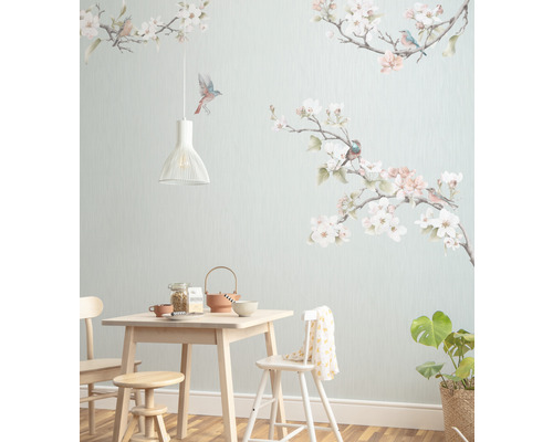 Jídelna se světlým dřevěným stolem, židlemi, stoličkou, nádobím, pokojovou rostlinou a nástěnnou tapetou s motivy ptáků a květin.