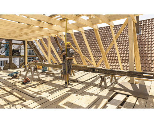 Stavební dělník měří střešní konstrukci měřicím nástrojem.