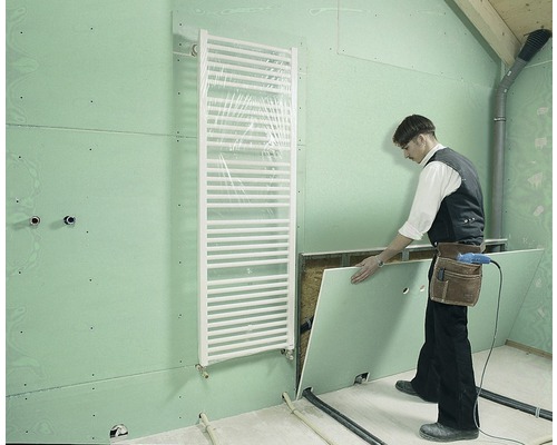 Řemeslník instaluje sádrokartonovou desku v koupelně s radiátorem.