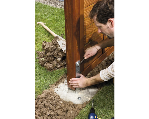 Muž montuje sloup plotu s klíčem na betonový základ v zahradě.