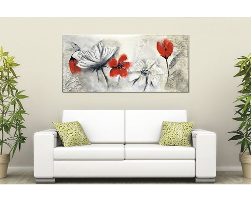 Obraz s květinami nad bílou pohovkou ve světlé místnosti.