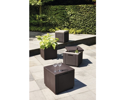 Venkovní scéna se čtyřmi hnědými ratanovými kusy nábytku: stolička s čalouněním, květináč s rostlinou, stůl se dvěma sklenicemi na víno a stůl s nápoji.