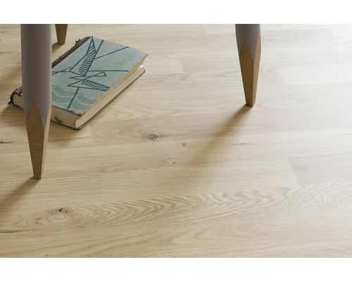 Světlá dřevěná podlaha s nohama stolu a knihou