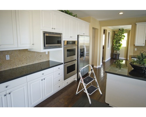 Kuchyňská scéna s bílými skříněmi, mikrovlnnou troubou, troubou, chladničkou a schůdky.