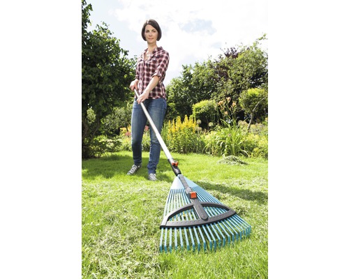 Žena používá hrábě na listí na zahradě k hrabání trávy.