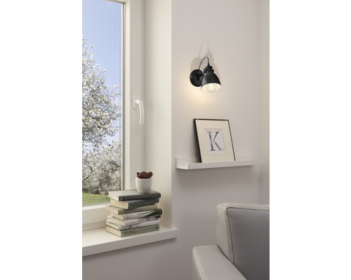 Obývací pokoj s oknem, hromadou knih a nástěnným svítidlem