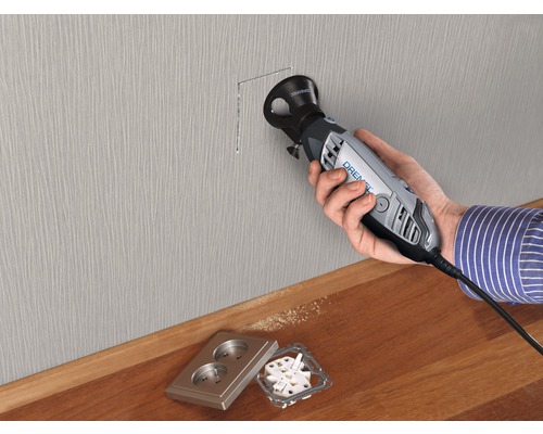 Osoba vyřezává otvor do zdi pro zásuvku pomocí Dremel Multi-Max.