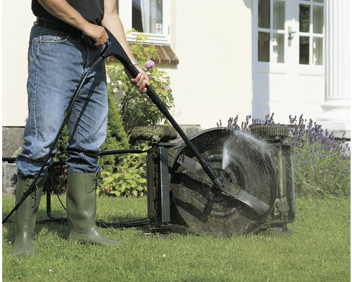 Osoba čistí sekačku na trávu vysokotlakým čističem na zahradě.