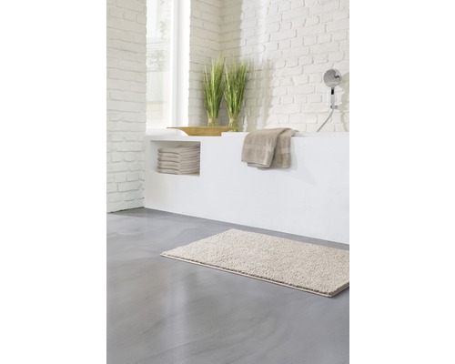 Světlá koupelna s koupelnovou předložkou, ručníky a dekorací na zděné vaně.