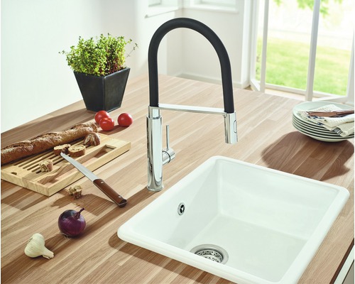 Kuchyňský dřez s vodovodní baterií obklopený potravinami na pracovní desce.