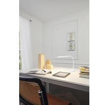 Psací stůl s lampou, zápisníkem, perem a dřevěnými figurkami ve světlém pokoji.