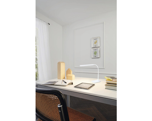 Psací stůl s lampou, zápisníkem, perem a dřevěnými figurkami ve světlém pokoji.