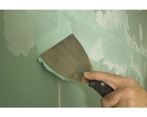 Řemeslník špachtlí sádrokartonovou stěnu špachtlí