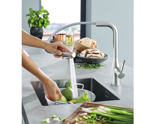 Kuchyňská scéna s dřezovou baterií a osobou myjící zeleninu