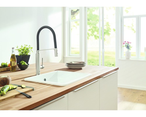 Kuchyňský dřez s baterií na pracovní desce s potravinami ve světlé kuchyni.